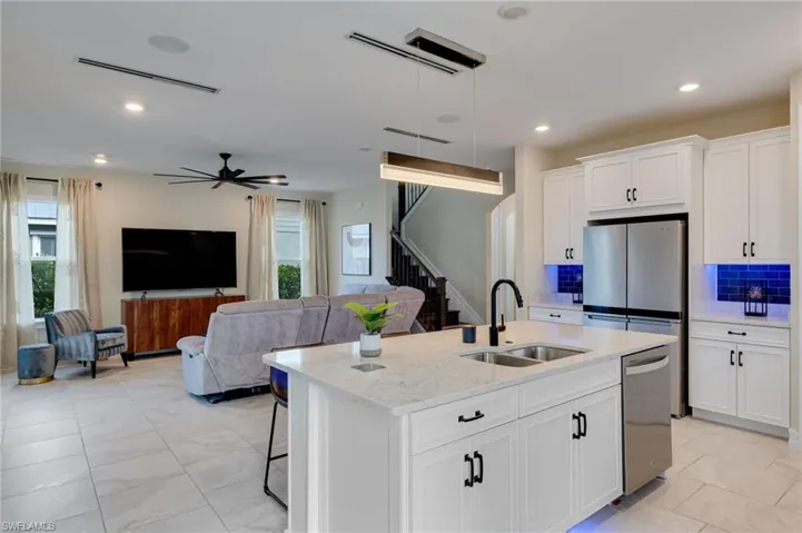 Kitchen with hanging light fixtures, white cabinets, open floor plan, a center island with sink, and light stone countertops