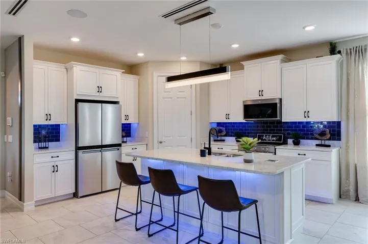 Kitchen featuring stainless steel appliances, white cabinetry, decorative backsplash, light stone counters, and recessed lighting
