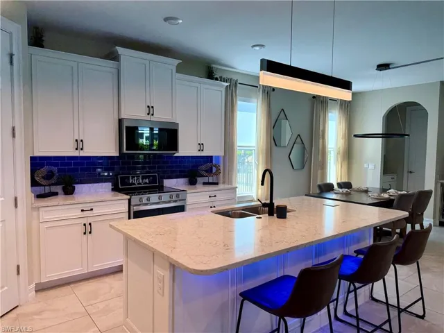 Kitchen with white cabinets, light stone counters, appliances with stainless steel finishes, and a center island with sink