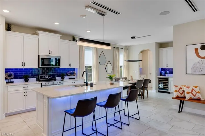 Kitchen featuring decorative backsplash, white cabinets, light stone countertops, appliances with stainless steel finishes, and recessed lighting
