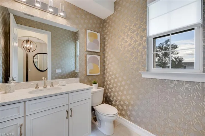 Downstairs Entry Half bathroom with wallpapered walls, vanity, a chandelier, and light tile patterned floors
