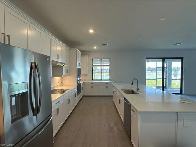 Kitchen with an island with sink, black appliances, dark hardwood / wood-style flooring, sink, and white cabinets