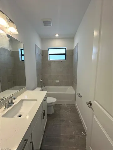 Full bathroom with tiled shower / bath, vanity, and toilet
