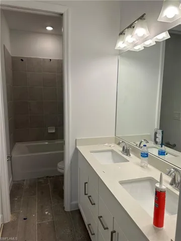 Full bathroom featuring dual bowl vanity, toilet, and tiled shower / bath combo