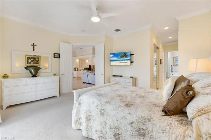 Carpeted bedroom with ensuite bath, ceiling fan, and crown molding