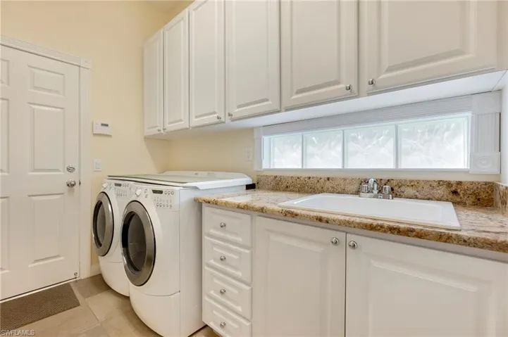 Washroom with washing machine and dryer, sink, light tile patterned floors, and cabinets