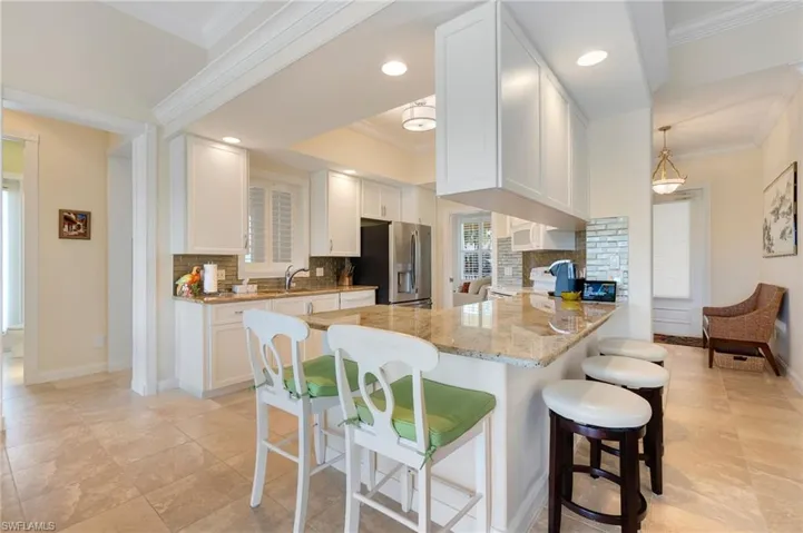 Kitchen with stainless steel refrigerator with ice dispenser, kitchen peninsula, decorative light fixtures, decorative backsplash, and white shaker cabinets