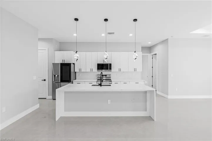 Kitchen with light stone countertops, stainless steel appliances, an island with sink, white cabinetry, and pendant lighting