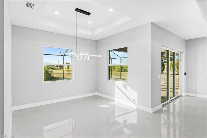 Empty room with healthy amount of natural light, a tray ceiling, recessed lighting, and a chandelier