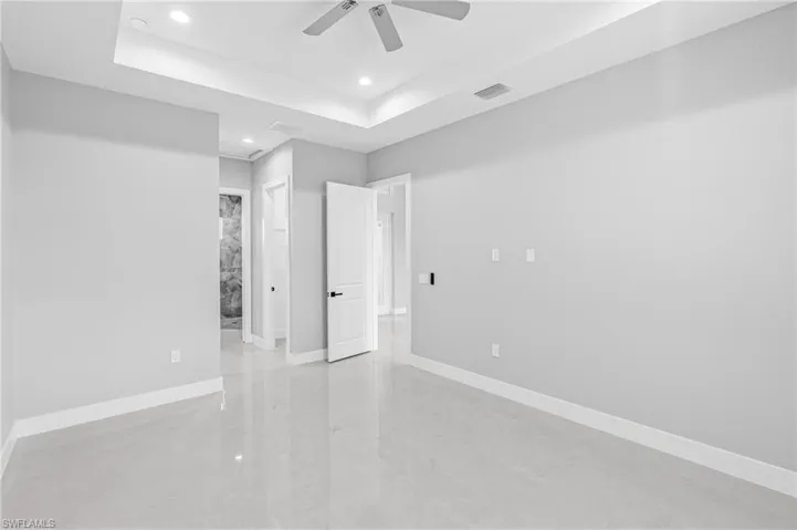 Unfurnished bedroom with a raised ceiling, recessed lighting, ceiling fan, and connected bathroom