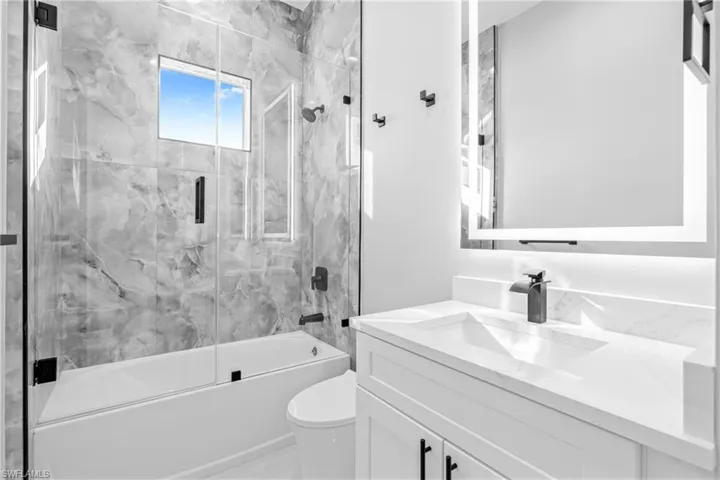 Bathroom with bath / shower combo with glass door, vanity, and marble finish floors