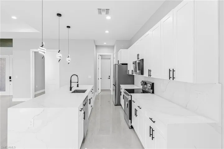 Kitchen featuring light stone counters, appliances with stainless steel finishes, decorative light fixtures, a spacious island, and recessed lighting