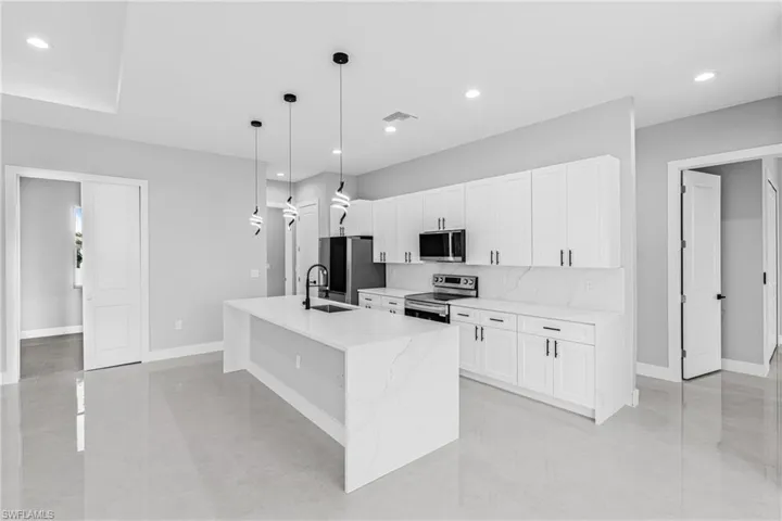 Kitchen featuring appliances with stainless steel finishes, light stone countertops, decorative light fixtures, white cabinetry, and a center island with sink