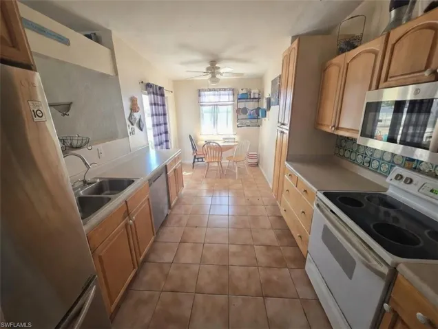 Kitchen featuring stainless steel appliances, light countertops, light tile patterned floors, a ceiling fan, and decorative backsplash
