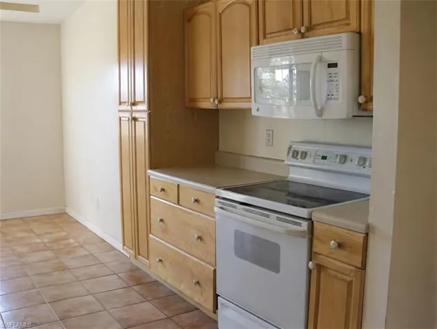 Kitchen with white appliances, light countertops, light tile patterned floors, and wood finish cabinets