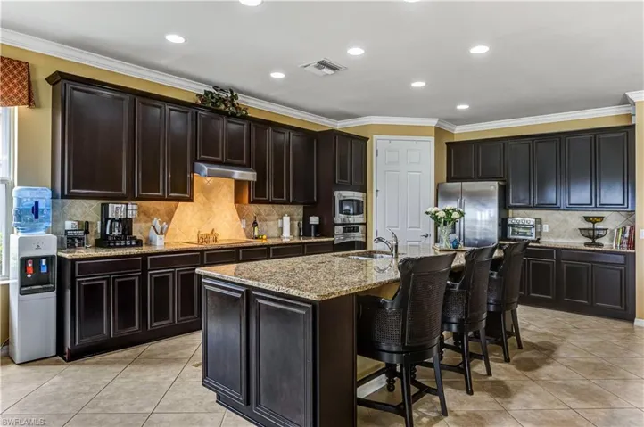 Kitchen featuring decorative backsplash, ornamental molding, light tile patterned floors, appliances with stainless steel finishes, and light stone counters