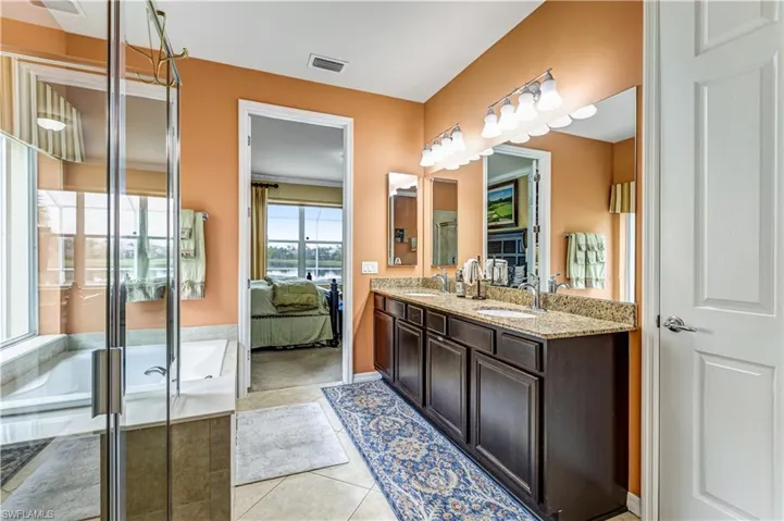 Full bathroom with ensuite bath, double vanity, a bath, light tile patterned floors, and a stall shower