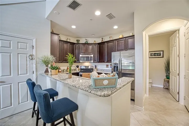 Kitchen with stainless steel appliances, dark brown cabinetry, a kitchen breakfast bar, light stone countertops, and a peninsula