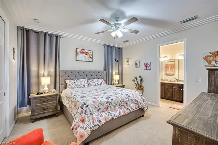 Bedroom with light carpet, ornamental molding, baseboards, ensuite bath, and a ceiling fan