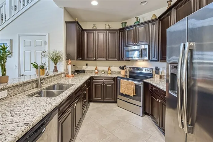 Kitchen featuring stainless steel appliances, a sink, light stone countertops, light tile patterned floors, and dark brown cabinets