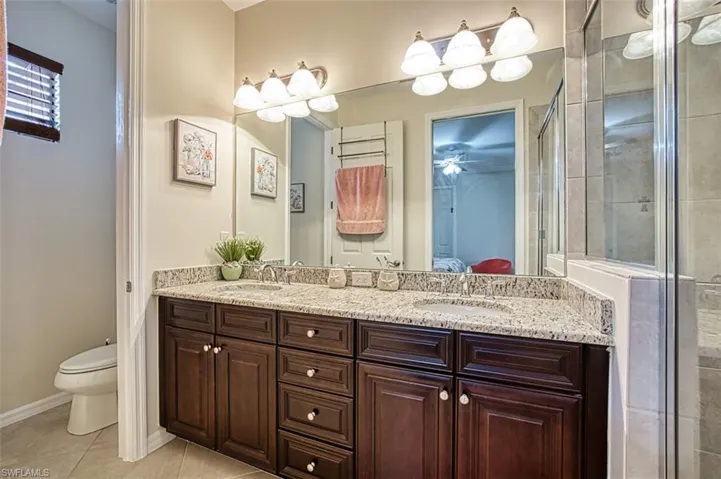 Ensuite bathroom with toilet, double vanity, a stall shower, tile patterned floors, and baseboards