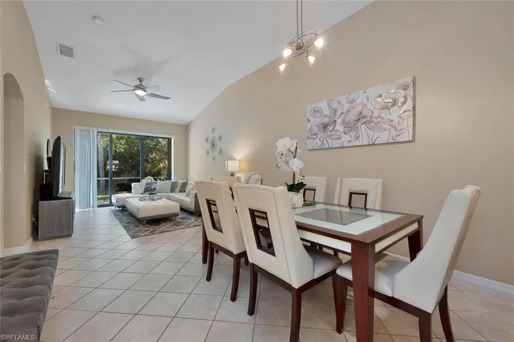 Tiled dining space featuring ceiling fan with notable chandelier and lofted ceiling