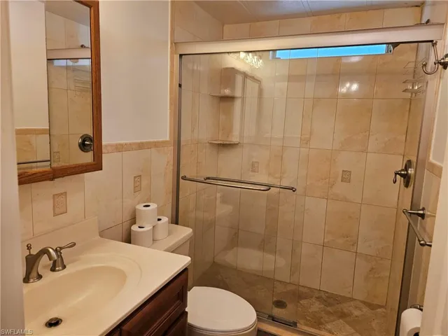 Bathroom with toilet, a shower with shower door, vanity, and tile walls