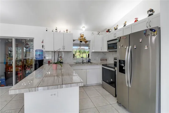 Kitchen with appliances with stainless steel finishes, light tile patterned flooring, sink, kitchen peninsula, and white cabinetry