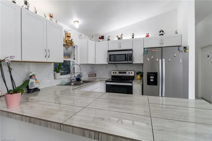 Kitchen featuring backsplash, white cabinetry, vaulted ceiling, sink, and stainless steel appliances