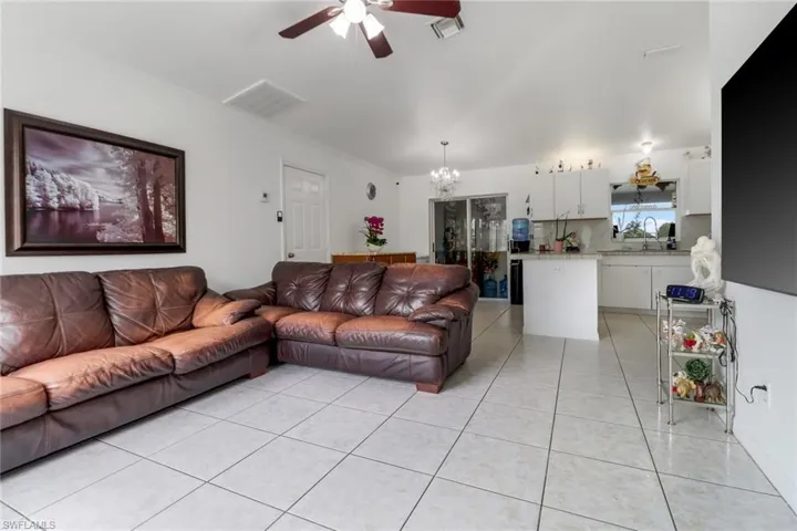 Living room with sink, crown molding, light tile patterned floors, and ceiling fan with notable chandelier