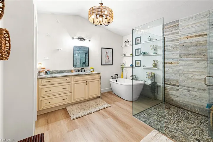 Light wood-finish flooring complements a freestanding soaking tub and a glass-enclosed shower with a pebble floor and natural stone-look wall tiles
