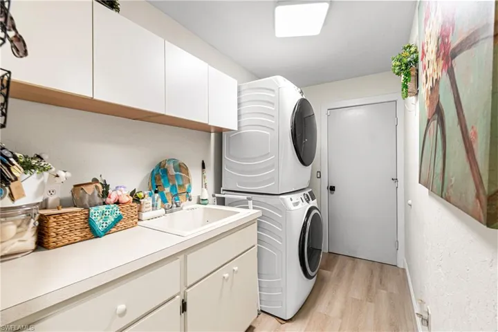 Dedicated laundry area featuring a stacked washer and dryer, white cabinetry, a built-in utility sink, and wood-finish flooring