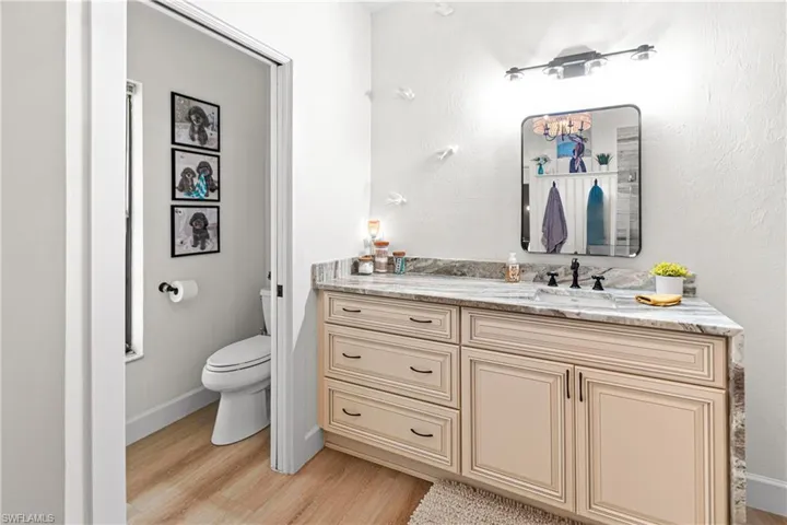 Bathroom vanity featuring a light-toned cabinetry, a stone countertop, an undermount sink with a matte black faucet, and a wall-mounted rectangular mirror
