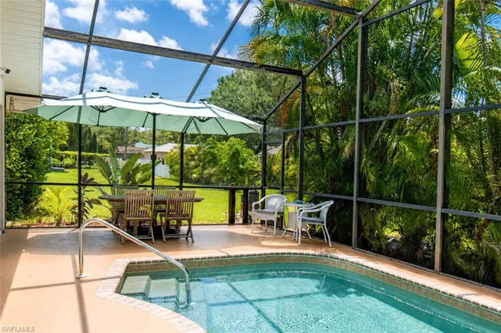 Screen-enclosed pool and patio area featuring a built-in spa with steps and a handrail
