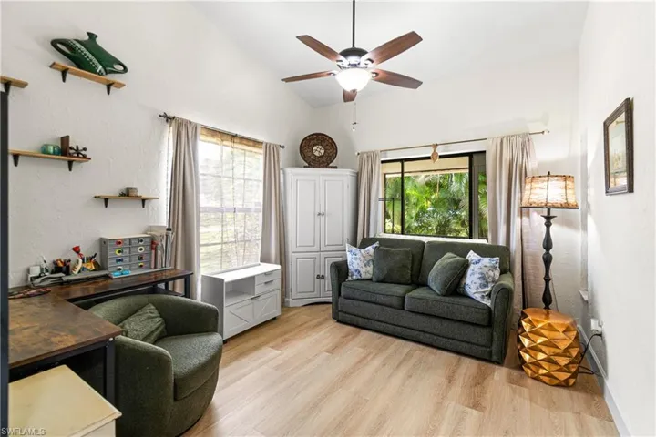 Vaulted ceiling with a ceiling fan, wood-finish flooring, built-in white cabinetry, large window with bamboo blinds, and floating wall shelves