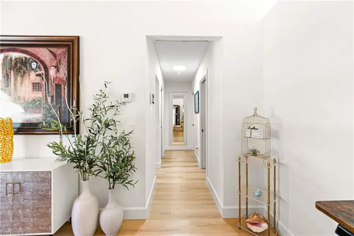 Bright hallway featuring wood-finish flooring, white walls, recessed lighting, and a continuous sightline