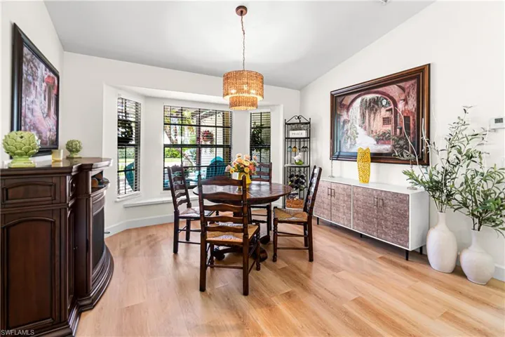 Dining area featuring a bay window, wood-finish flooring, a woven chandelier, built-in shelving, and white walls