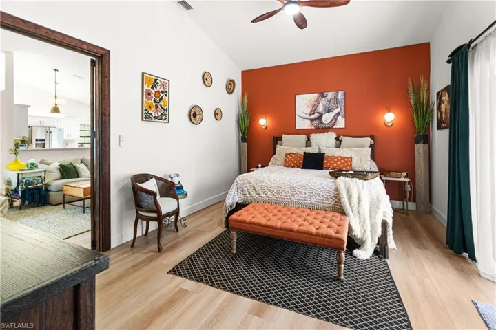 Spacious primary bedroom featuring vaulted ceilings, wood-finish flooring, a ceiling fan, and an accent wall