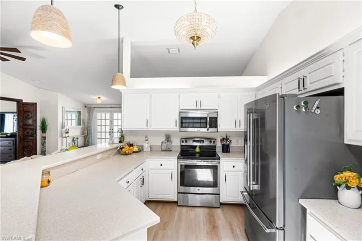 Kitchen featuring white cabinetry, stainless steel appliances, light-toned countertops, wood-finish flooring, and vaulted ceilings