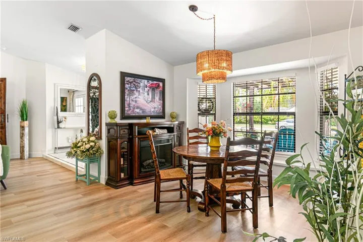 Dining area featuring a bay window with horizontal blinds, wood-finish flooring, a tiered woven pendant light, and a dark wood electric fireplace console