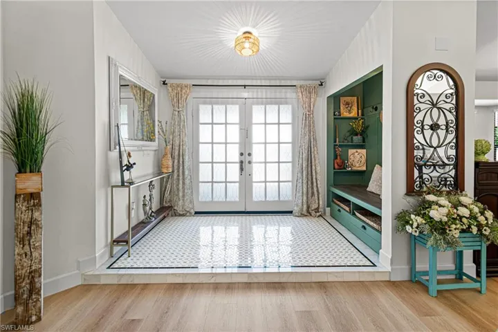 Entryway featuring white French doors, geometric pattern floor tile, a built-in bench with storage, recessed shelving, and a decorative arched ironwork accent
