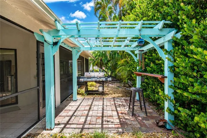Outdoor patio featuring a light blue pergola, brick paver flooring, and abundant surrounding foliage