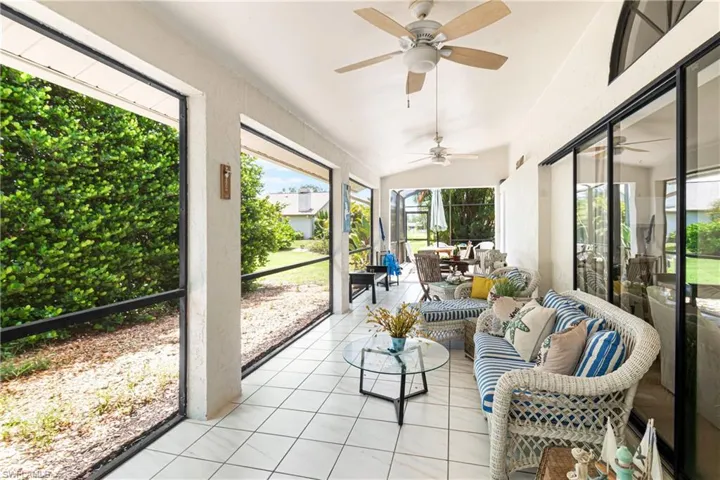 Screened patio featuring white tile flooring, multiple ceiling fans, and a high vaulted ceiling