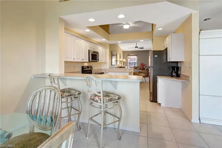 Kitchen with stainless steel appliances, light countertops, a ceiling fan, a peninsula, and a kitchen bar