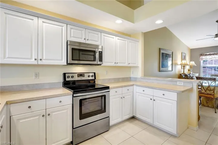 Kitchen featuring white cabinets, ceiling fan, a peninsula, stainless steel appliances, and light countertops