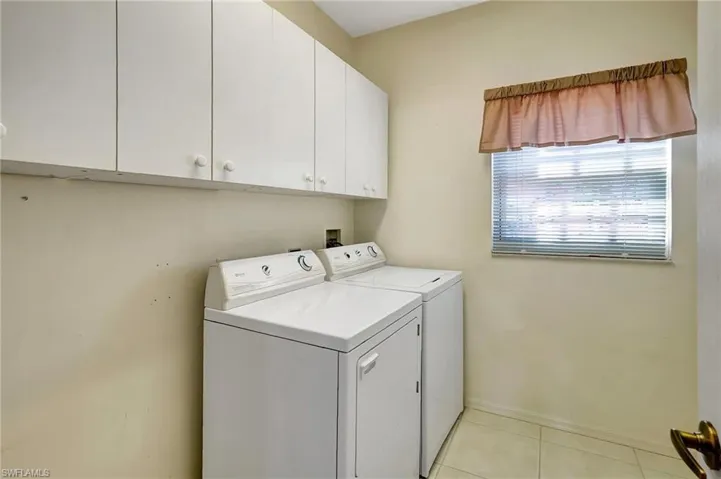 Laundry area featuring cabinet space, light tile patterned floors, baseboards, and independent washer and dryer