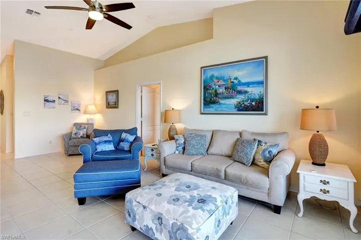 Living room featuring light tile patterned floors, visible vents, baseboards, ceiling fan, and vaulted ceiling