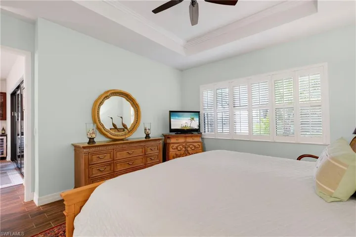 Bedroom featuring ceiling fan, crown molding, a tray ceiling, and ensuite bathroom
