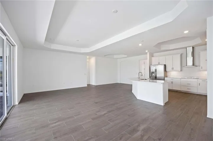 Kitchen featuring wall chimney range hood, a tray ceiling, a sink, and stainless steel fridge with ice dispenser