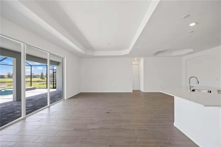 Unfurnished living room featuring a sink, a raised ceiling, recessed lighting, baseboards, and wood finished floors